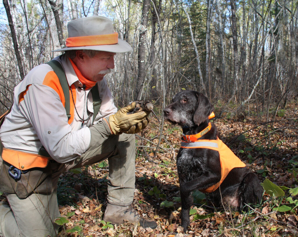 man holds harvested bird in front of dog